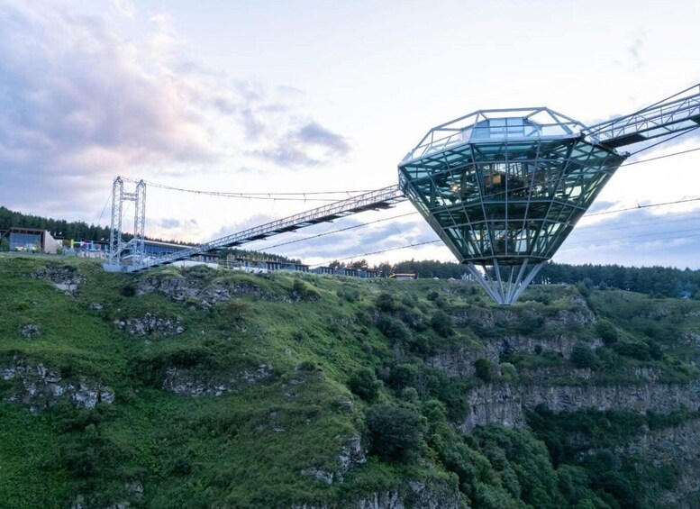A large geodesic dome structure on a hill with a suspension bridge in the background. 1