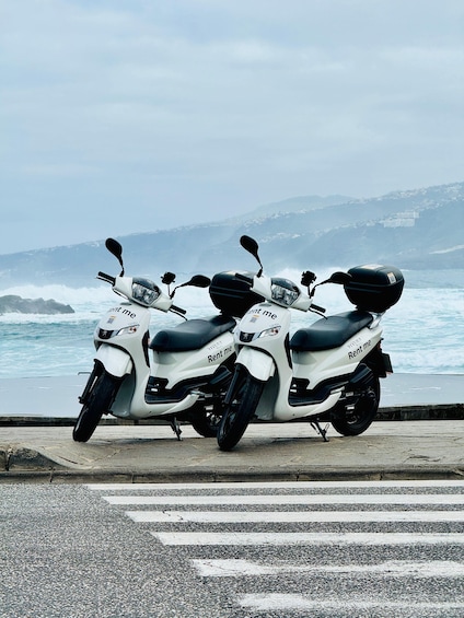 Three white scooters with 'Rent me' stickers parked by the sea. 3