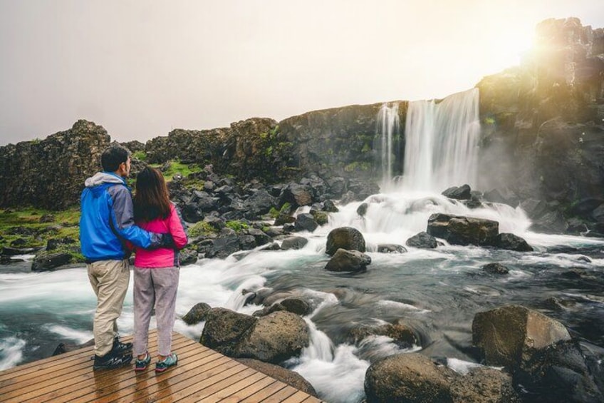A couple standing on a wooden deck overlooking a waterfall. 2