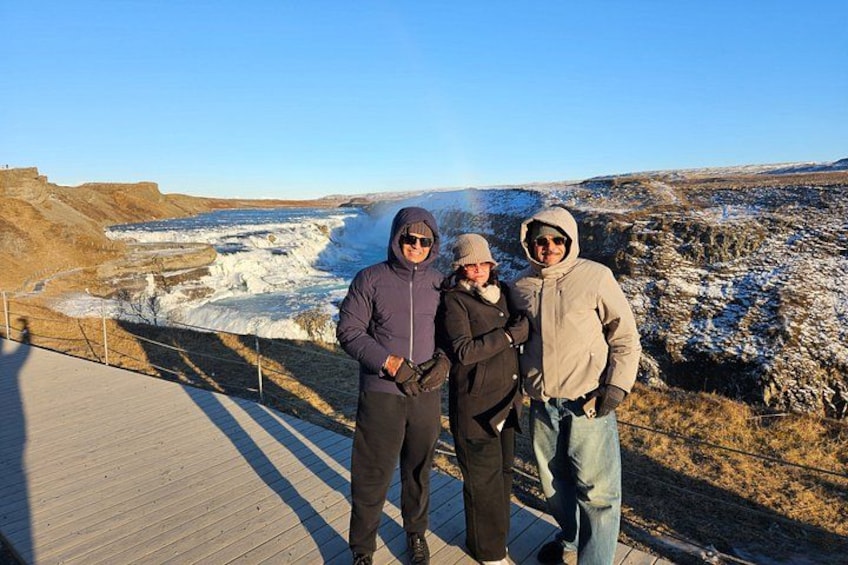 Three people standing on a wooden boardwalk overlooking a frozen landscape with a body of water. 1