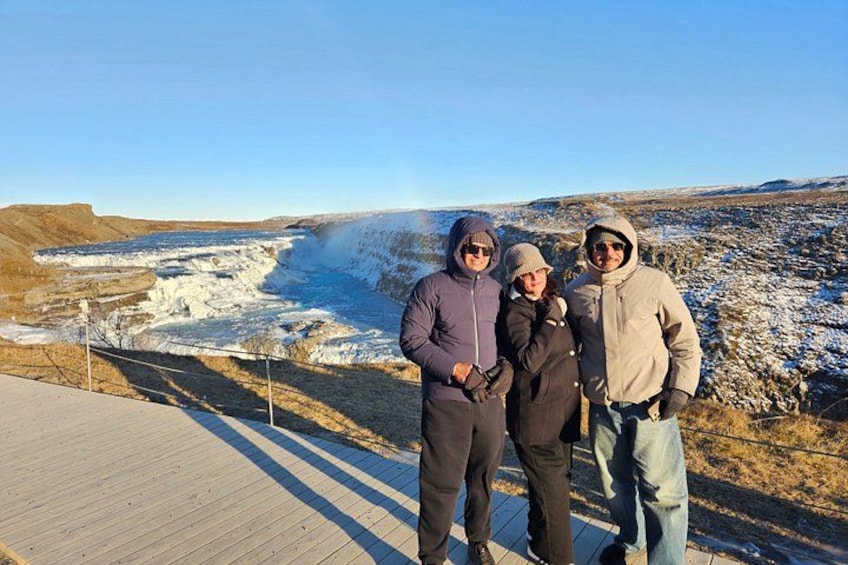 Tre persone in piedi su una passerella di legno con vista su un paesaggio innevato e un fiume. 1