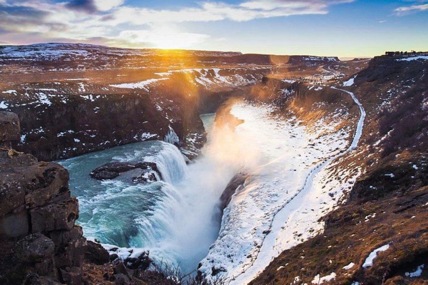 Una cascata che si getta da una parete rocciosa, circondata da paesaggi innevati e un cielo sereno. 2