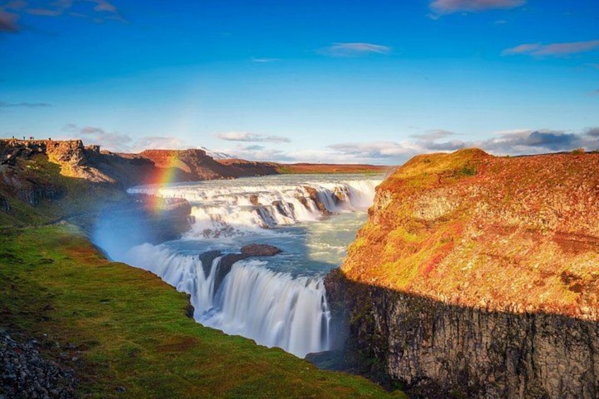 Una cascata che si getta da una rupe, con un arcobaleno sullo sfondo e un paesaggio erboso. 5