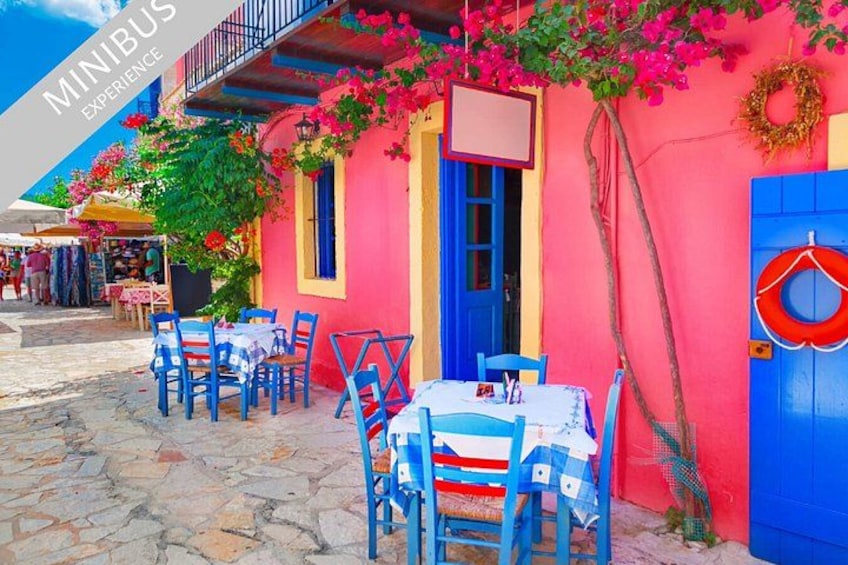 A colorful outdoor café with blue chairs and tables, a red door, and pink flowers. 1