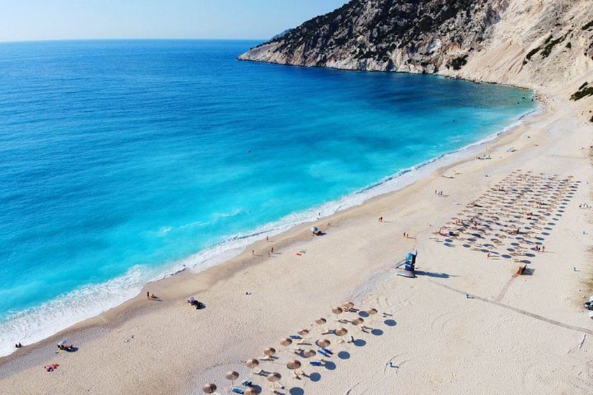 A beach with clear blue water, sandy shore, and rocky cliffs. 4