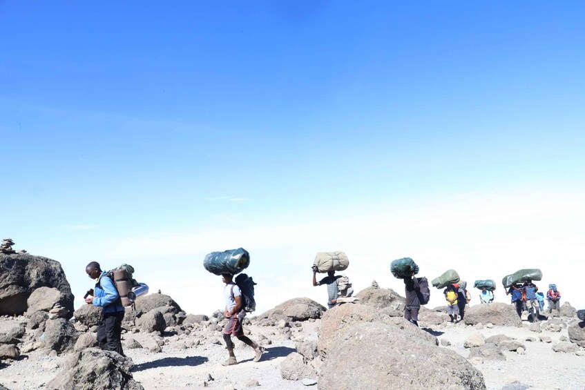 A group of people carrying large loads across a rocky terrain. 5