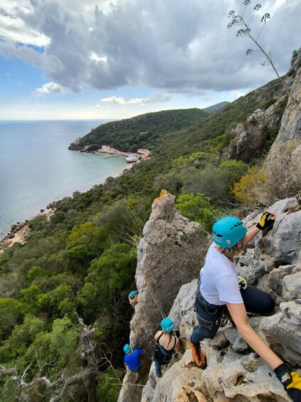 A person climbing a rocky cliff with a coastal view. 1