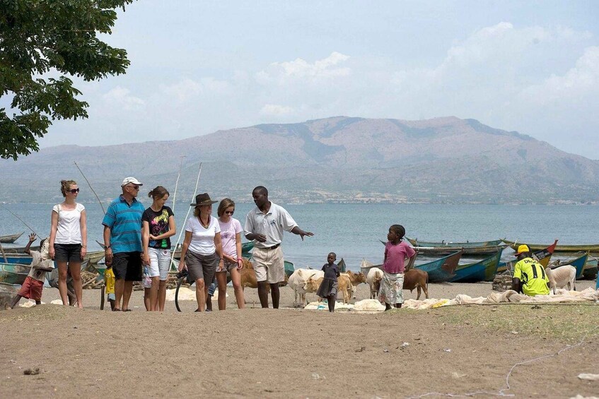 A group of people by a lake with boats and cattle in the background. 3