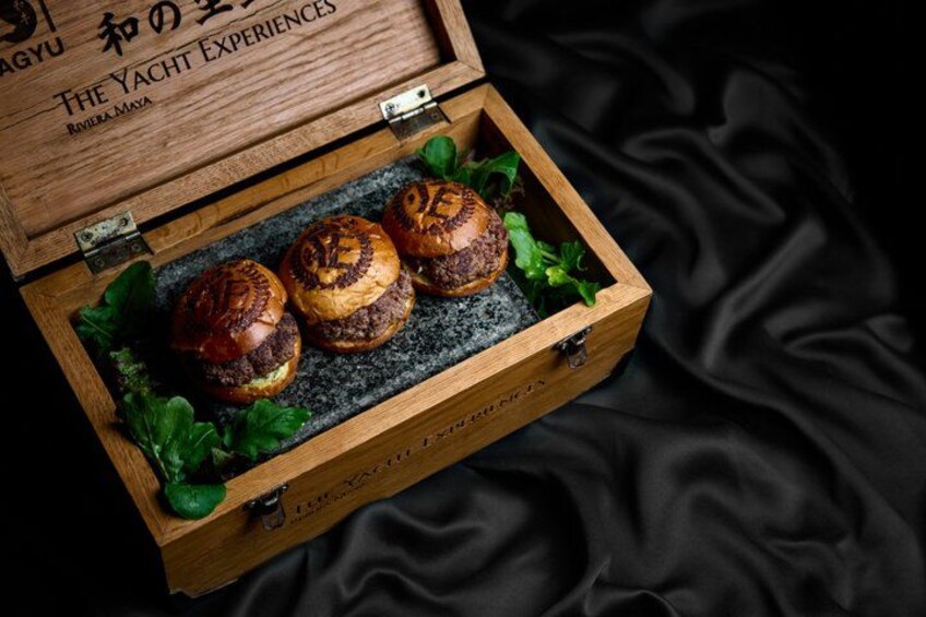 A wooden box with three burgers on a bed of greens, placed on a black fabric. 2