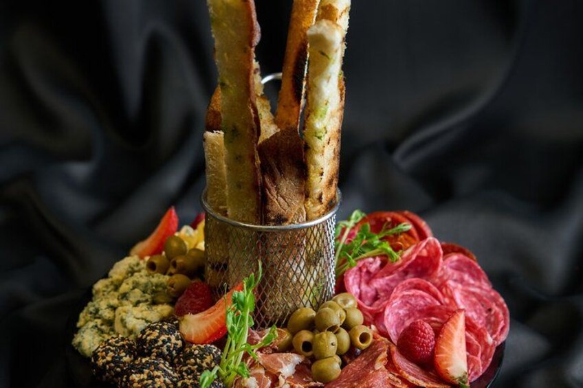 A charcuterie board with breadsticks, olives, strawberries, and various meats. 3