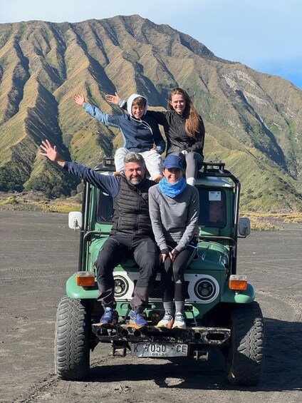 A group of people on a green off-road vehicle with a mountainous landscape in the background. 5