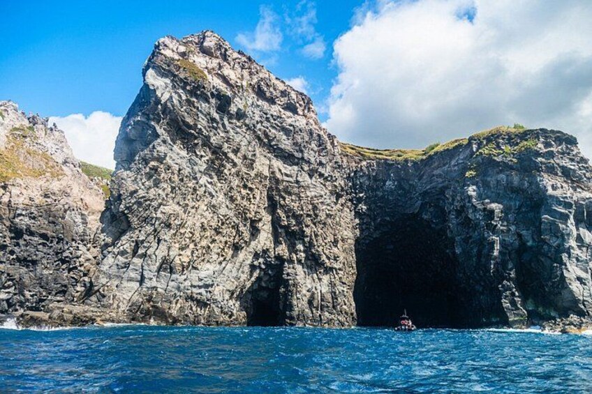 Un paisaje costero rocoso con la entrada grande de una cueva y un bote en el agua. 2