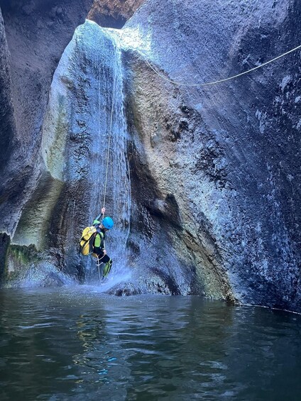 A person rappelling down a waterfall in a rocky canyon. 1