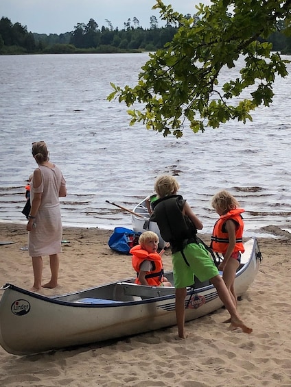 A group of people preparing a canoe on a sandy beach near a lake. 3