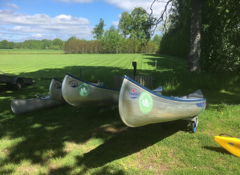 Three canoes with logos resting on grass near a golf course. 5