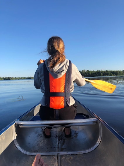 A person in a canoe wearing a life jacket, paddling on a calm body of water. 2