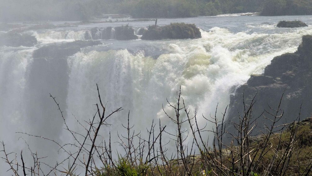 A powerful waterfall with turbulent water, surrounded by rocky terrain and sparse vegetation. 4