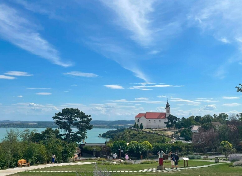 A church with a red roof and a tower, surrounded by greenery and a lake. 2