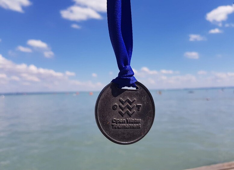 A medal with 'Open Water Swimming' engraved on it, hanging against a backdrop of a clear blue sky and calm sea. 5