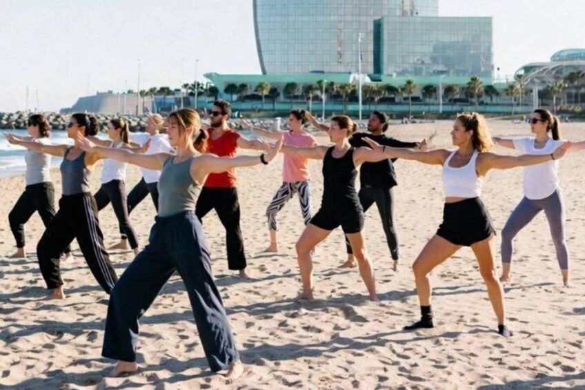 Un grupo de personas realizando una rutina de ejercicios sincronizada en una playa arenosa, con un edificio moderno al fondo. 5