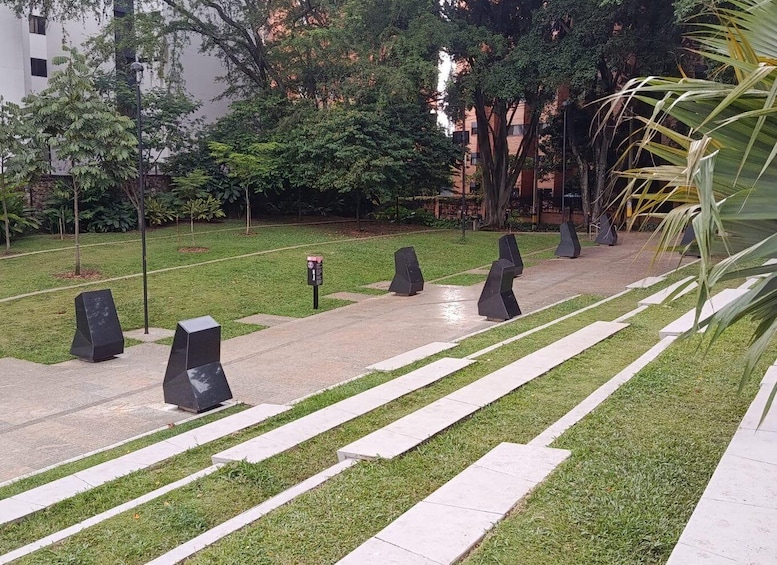 A landscaped area with a pathway, grass, trees, and modern buildings in the background. 4