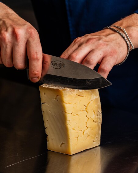 A person cutting a large block of cheese with a Sanellia knife. 1