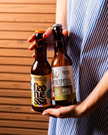 Two bottles of beer held by a person wearing a striped shirt. 2