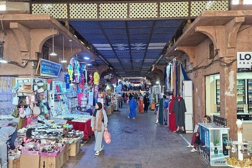 An indoor market with various stalls selling goods, a signboard, and a ceiling with a lattice design. 4