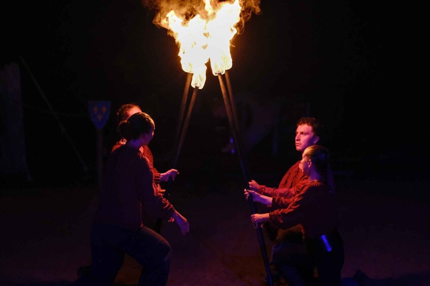 Two individuals performing a fire act with a large fire on a stand. 2