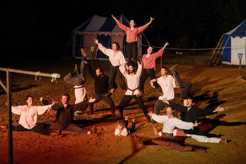 A group of people in historical costumes performing an outdoor dance in a dirt field with tents in the background. 5