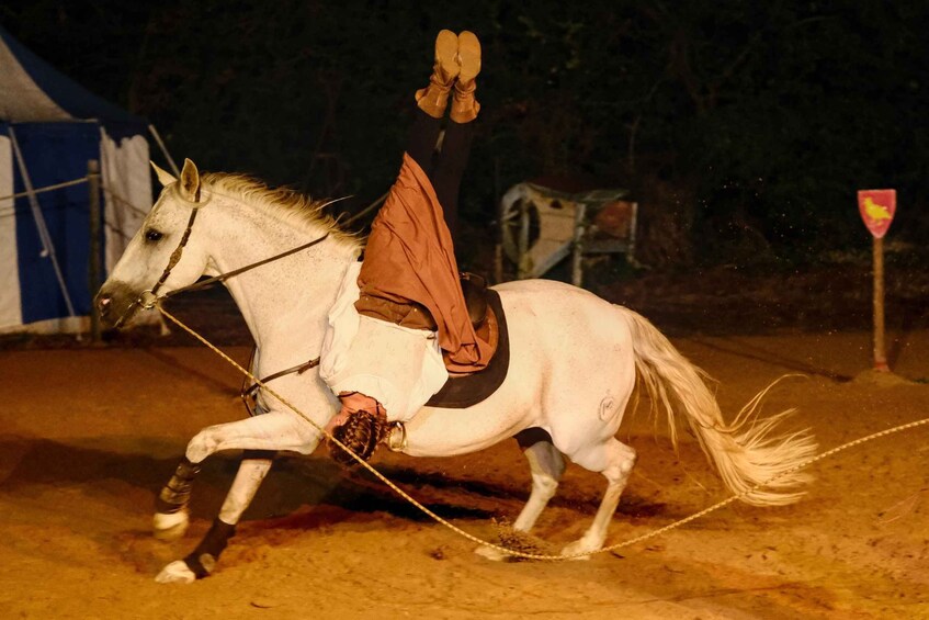 A person riding a white horse in a sandy arena with a blue tent in the background. 5