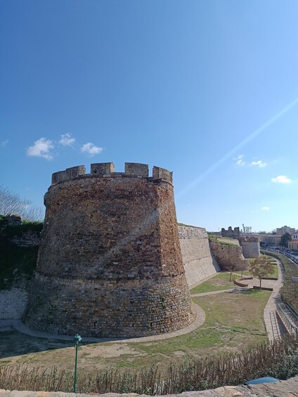 A historic stone castle with a circular tower, surrounded by a grassy area and a paved walkway. 5