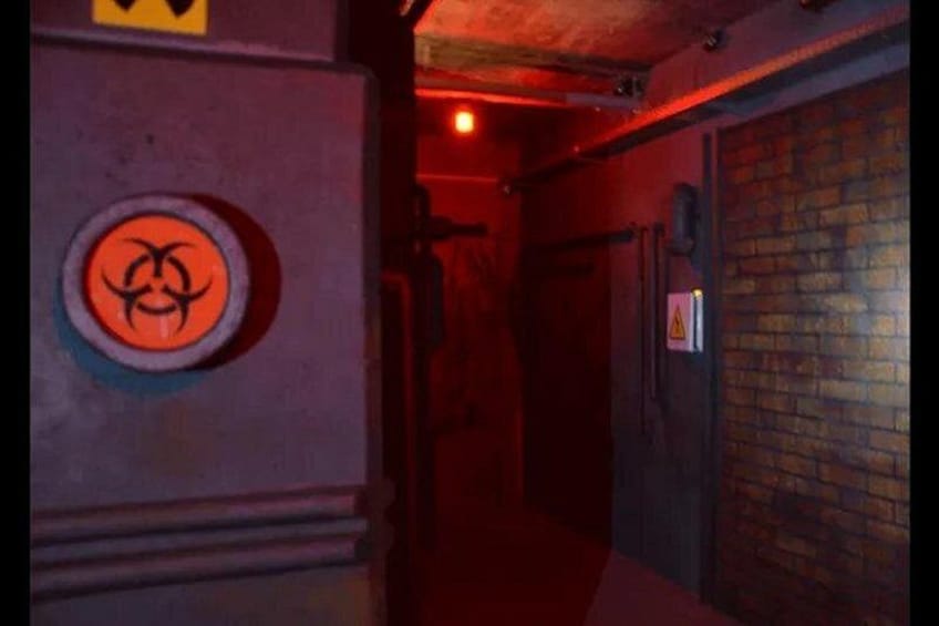 Un corridoio scarsamente illuminato con un simbolo di rischio biologico sul muro e un muro di mattoni alla destra. 5
