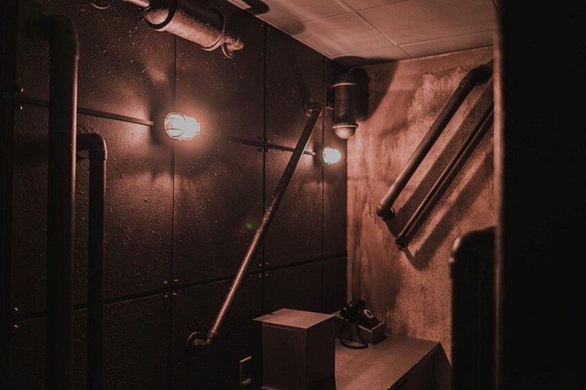 Una stanza poco illuminata con una parete in legno, un tubo metallico e un lampadario. 1