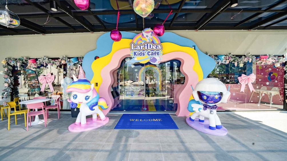 A colorful entrance to LariDea Kids' Cafe with a 'Welcome' mat, two unicorn statues, and a vibrant archway. 1