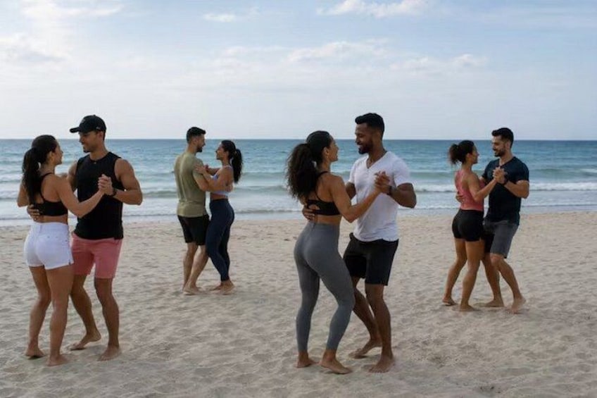 A group of people dancing on a beach with the ocean in the background. 2
