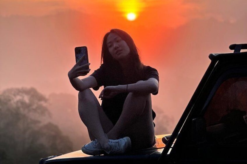 Una persona seduta sul cofano di un'auto, con un tramonto sullo sfondo. 5