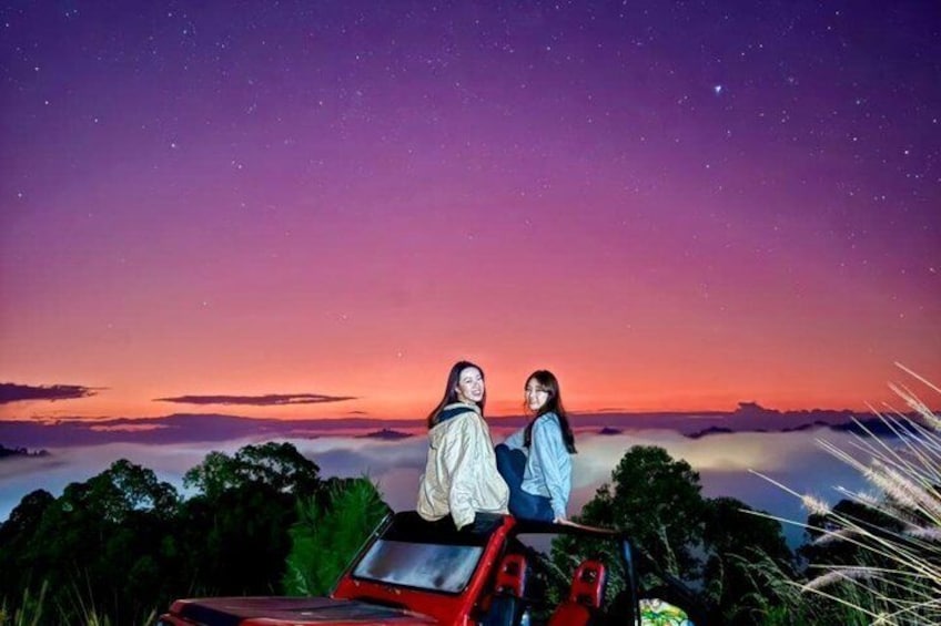 Due persone sedute su un veicolo rosso, con vista su un cielo stellato e un paesaggio con alberi e un orizzonte lontano. 3