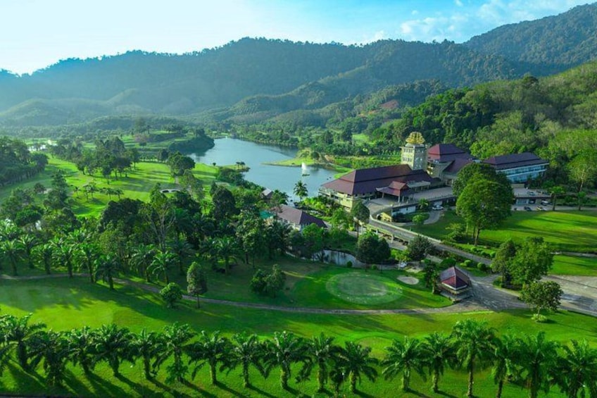 A golf course with a lake, a large building with a tower, and surrounding hills. 3