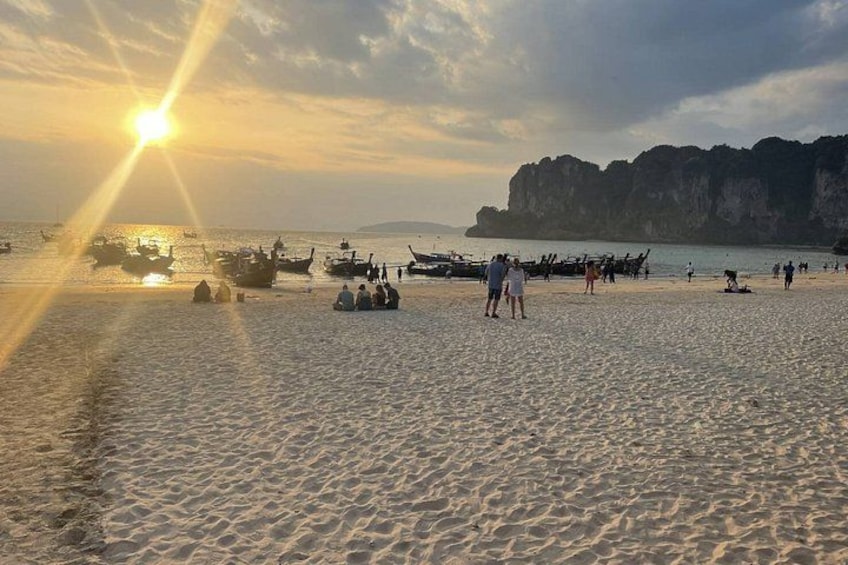 A beach with boats, people, and a sunset. 4