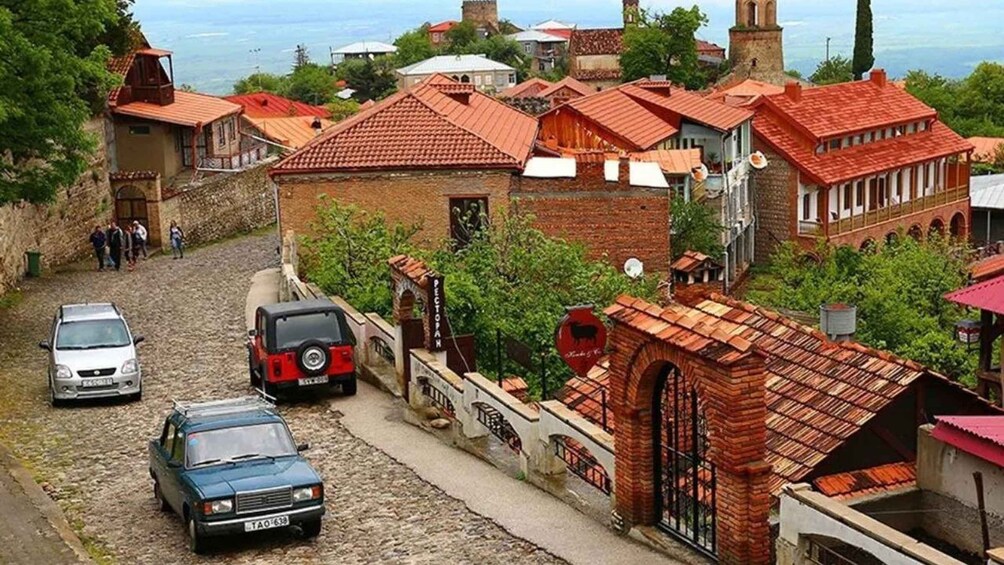 A cobblestone street with traditional red-roofed buildings, a brick archway, and parked cars. 2