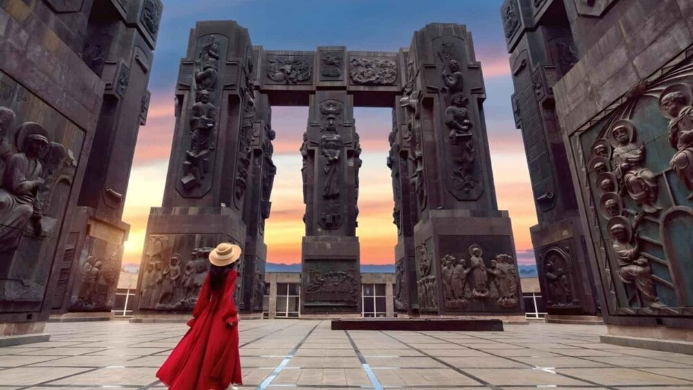 A person in a red dress standing in front of a large, ornate gateway with intricate carvings. 4