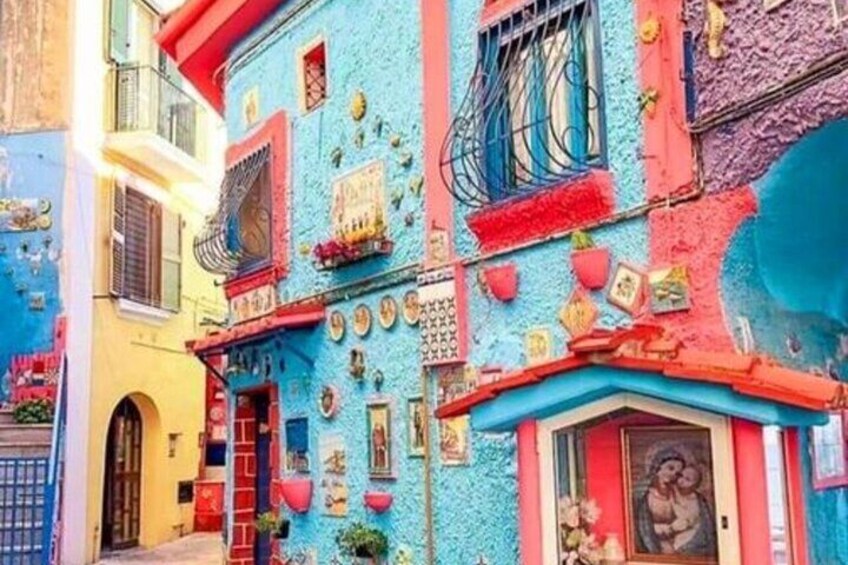 A colorful building with vibrant blue and pink walls, decorative plates, and a small shrine. 3