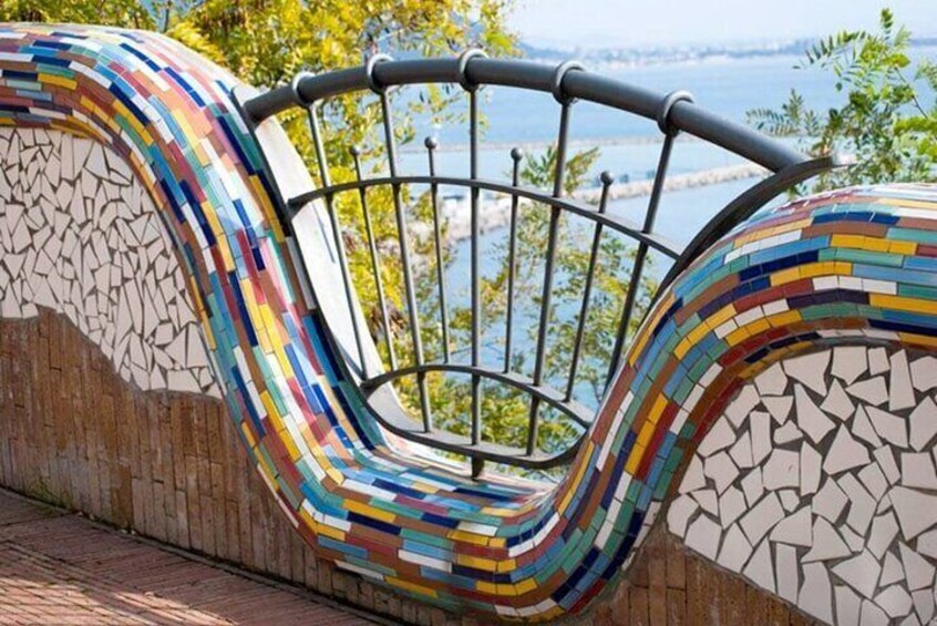 A colorful mosaic bench with a metal railing overlooking a body of water. 2