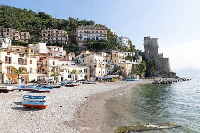 A coastal town with buildings on a hillside, a beach with boats, and a castle-like structure. 5