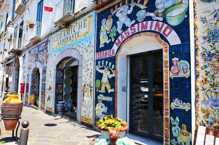 A street with colorful ceramic shop fronts, including 'CERAMICHE ARVENANTE' and 'CERAMICA MASSIMINO.' 1