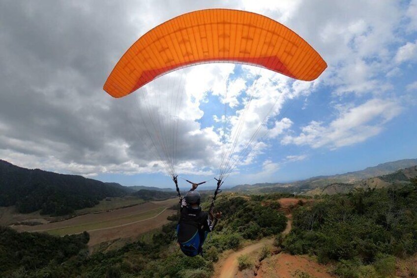 Een paraglider met een oranje vlieger over een heuvelachtig landschap. 1