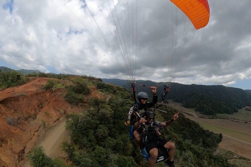 Iemand paraglidet boven een glooiend landschap met schaarse vegetatie en een bewolkte lucht. 4
