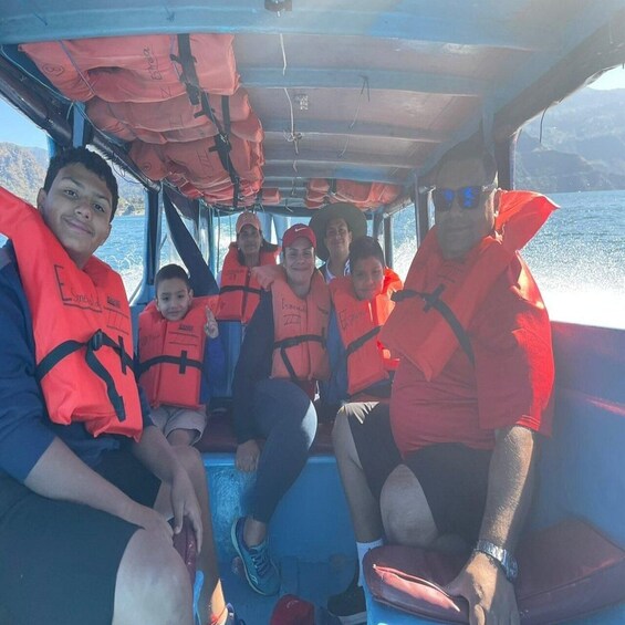 Een groep mensen in een boot, allen met reddingsvesten, met water zichtbaar door de ramen. 2