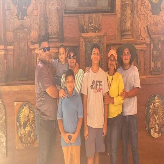 Een groep mensen poseert voor een decoratieve muur met ingewikkelde houtsnijwerken en religieuze kunst. 5